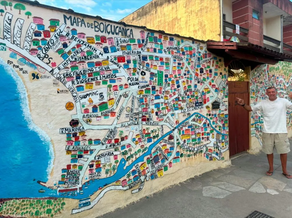 Eduardo Camarini posa em frente ao mapa de Boiçucanga que pintou no muro de sua casa, unindo criatividade e amor pelo bairro.